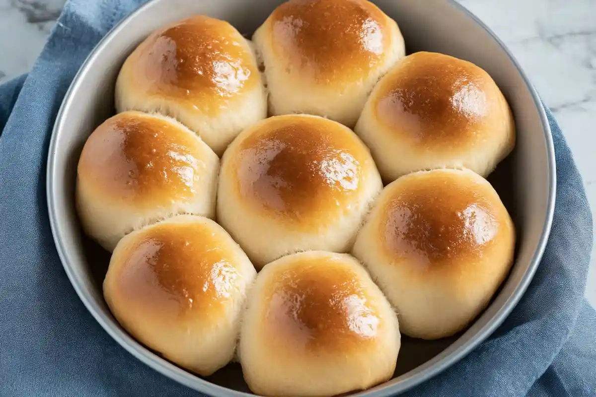 A round pan filled with golden-brown sourdough dinner rolls, perfectly soft and fluffy with a glossy, buttery finish.