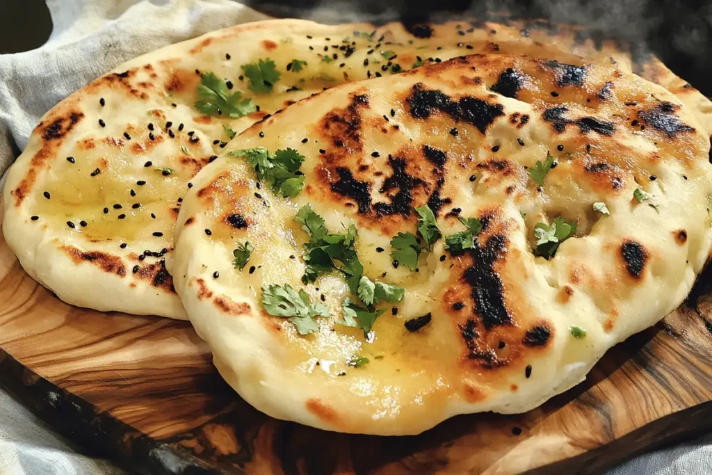 Golden sourdough discard naan brushed with melted butter, sprinkled with cilantro and black sesame seeds on a wooden serving board.